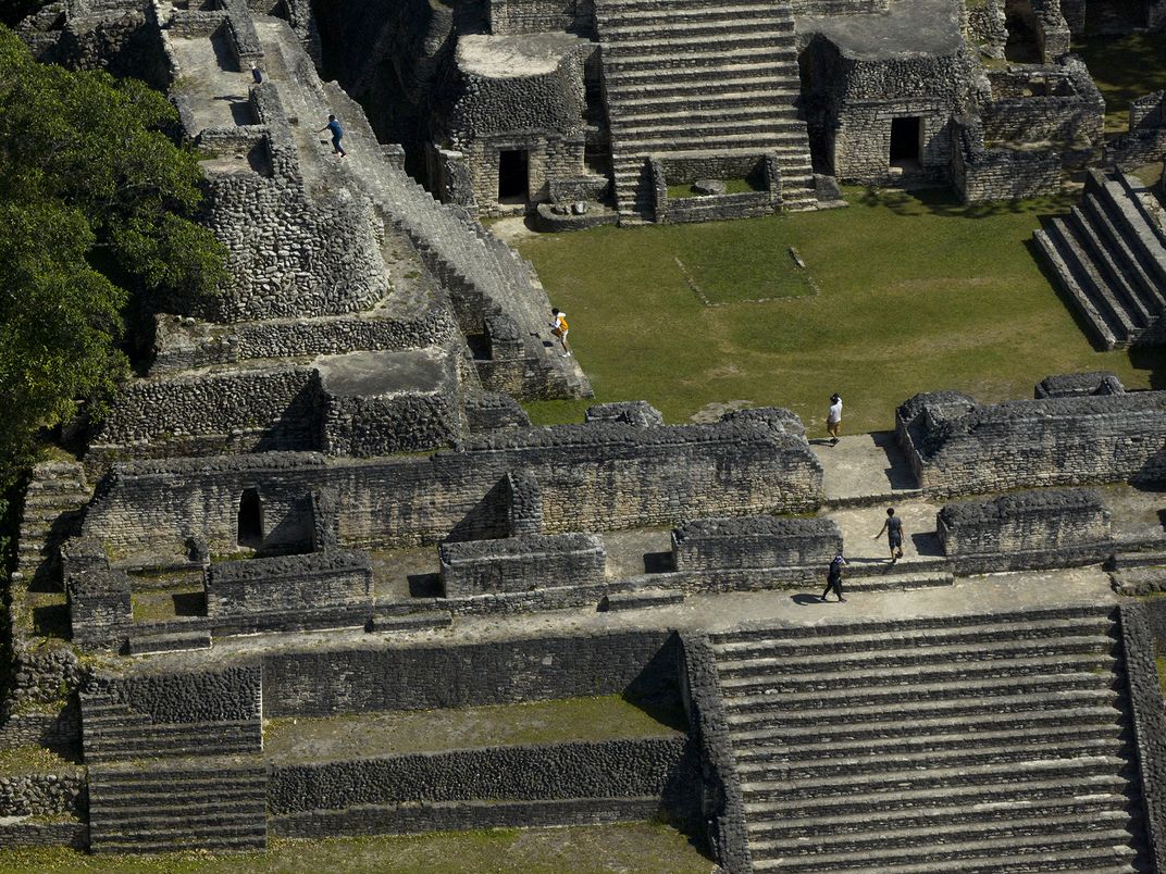 Tourists climb to the top of Caana. The complex is built in the triadic style common in Meso- america: The central building is flanked by two smaller temples, with other pyramids and buildings surrounding the elevated area.