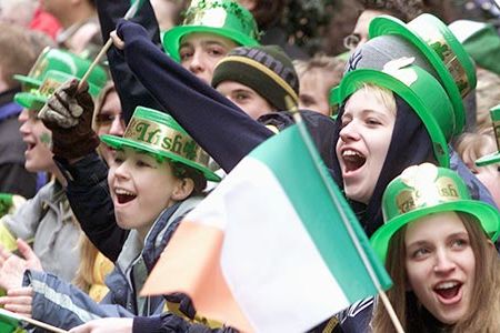 Group of people cheering and waving Irish flags during the St. Patrick's Day parade in New York City.