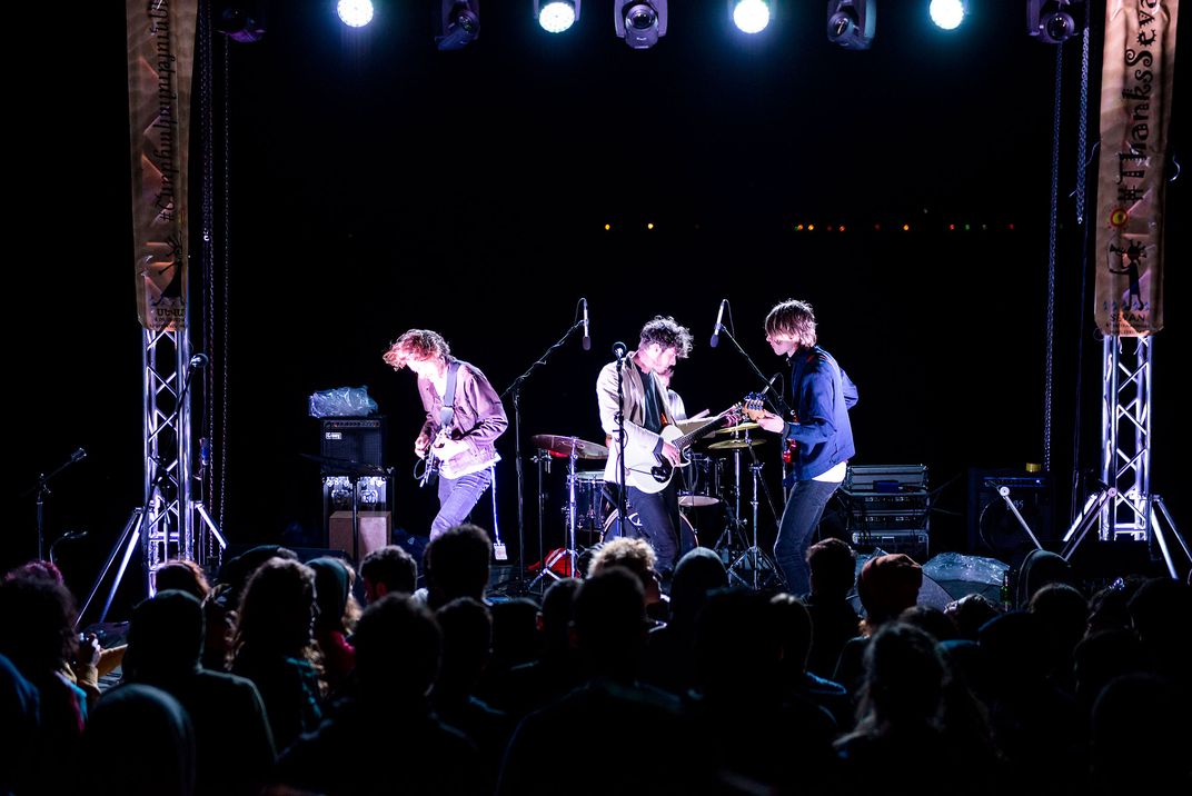 Three musicians stand together on a darkly lit stage. They appear to be moving, dancing with the music.