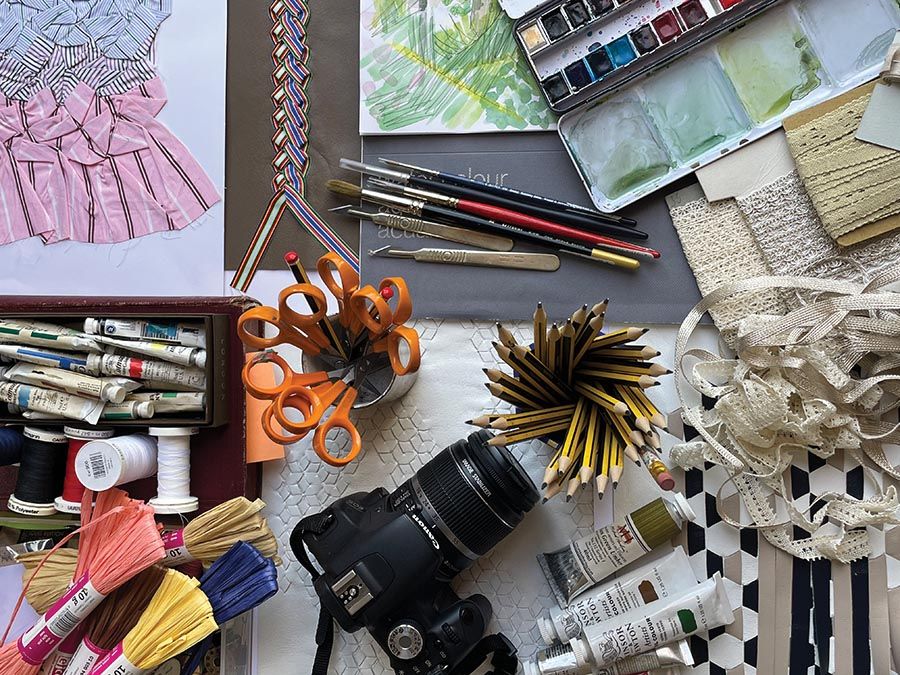A variety of tools used to create art are displayed including scissors, fabric, a digital camera, tubes of paint and paintbrushes