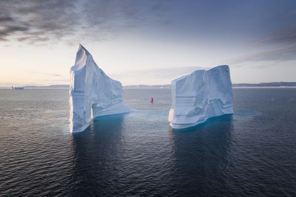 Red sailboat next to a massive iceberg in Greenland thumbnail
