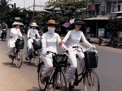 Ao dais make striking uniforms for four university students heading home after classes. Long gloves and hats provide welcome protection from the sun in a land where a suntan is not considered fashionable; masks serve as barriers to dust and exhaust.