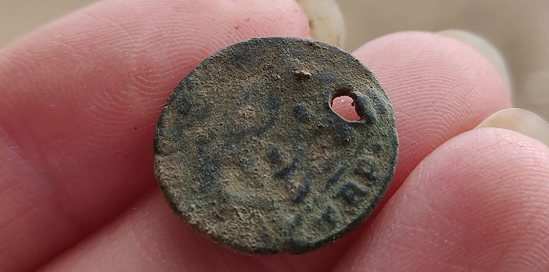 picture of hand holding rusted dirty coin with hole from Roman empire