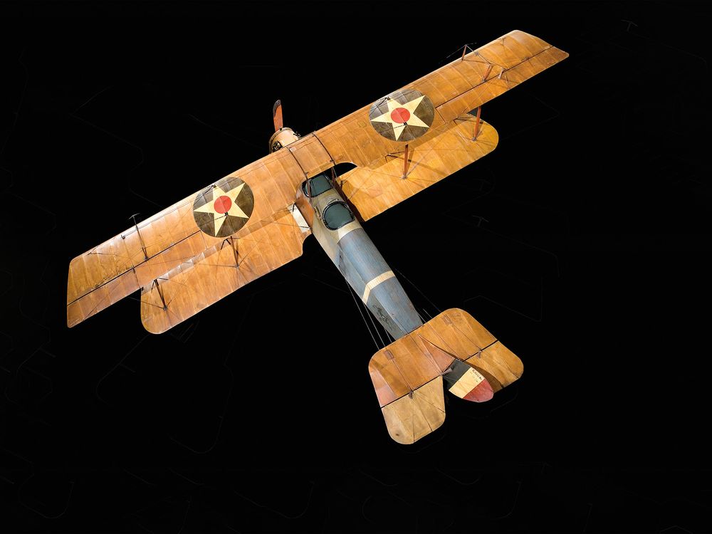 A wood and fabric World War I-era Curtis JN-4D aircraft is on display at the National Air and Space Museum. It has tan wings, and a brown and blue fuselage.