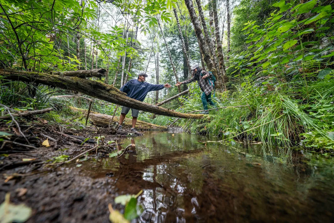 Two people crossing a river in a forest