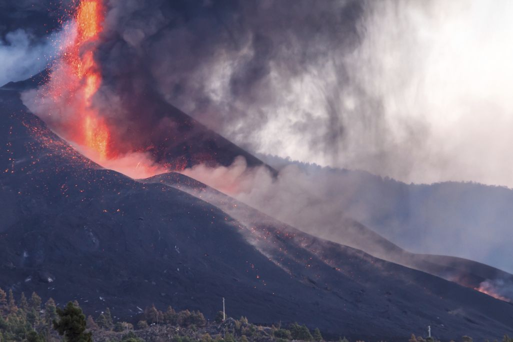 An image of the La Palma volcano erupting. A fountain of lava is seen spewing from the mountain.