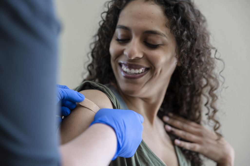Photo of Black woman receiving a vaccine from a doctor with a bandaid on her arm