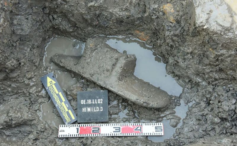 stone grinding slab in mud with a ruler—looks about six inches across