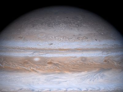 Jupiter's moon Io in orbit around the gas giant. Io is casting a dark shadow on Jupiter's atmosphere.