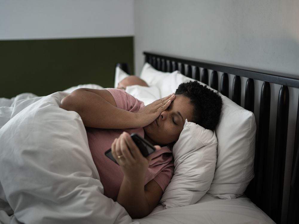 A woman lays in bed and looks at her phone