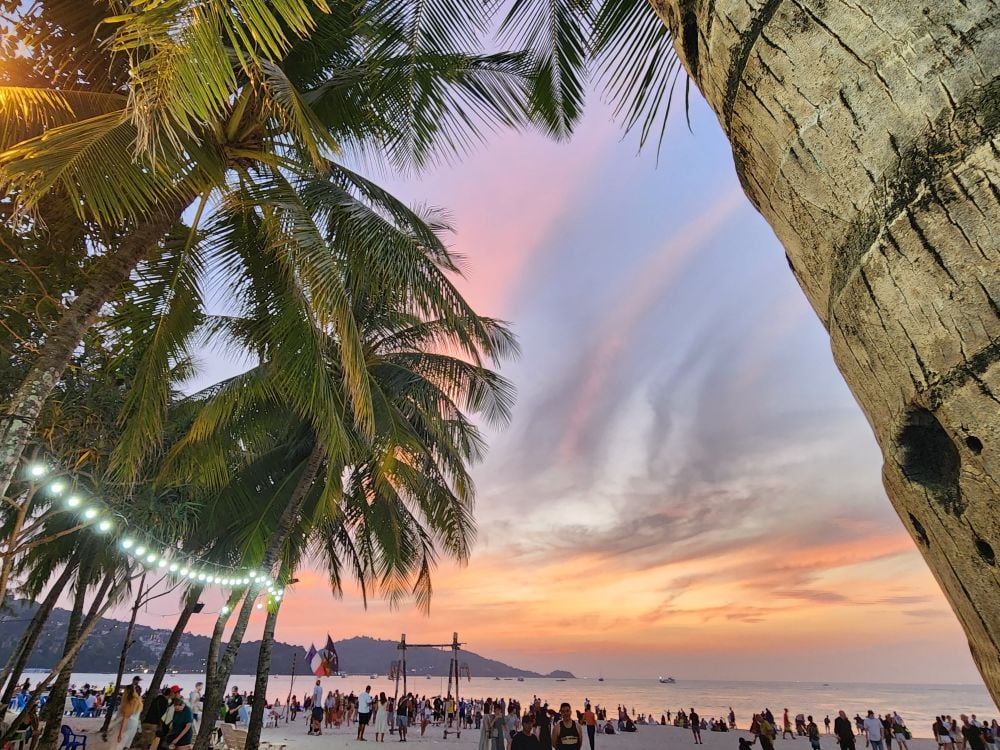 The colorful sky of Patong Beach just before dusk is seen through the palm trees.
