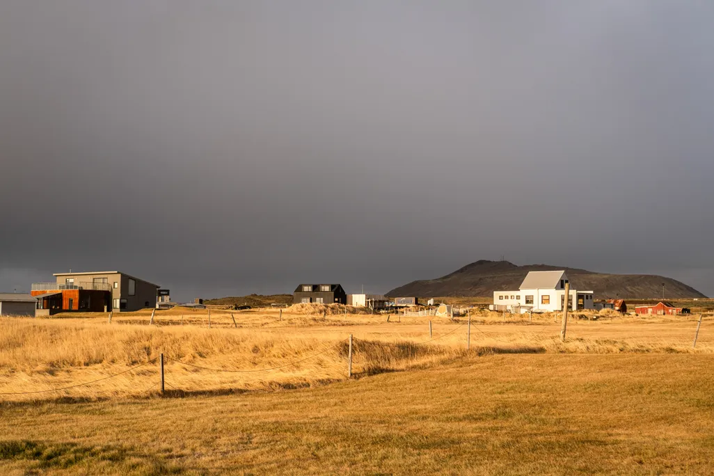 A couple of buildings at the back of a field with a dark sky overhead