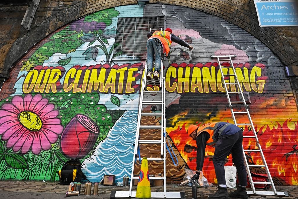An colorful mural that reads "our climate in changing" with two people painting