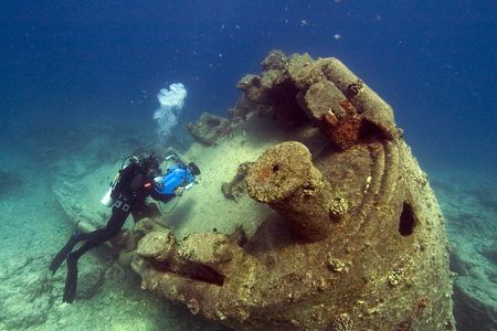 A diver uses a camera to study a barnacle-covered submarine resting on the seafloor