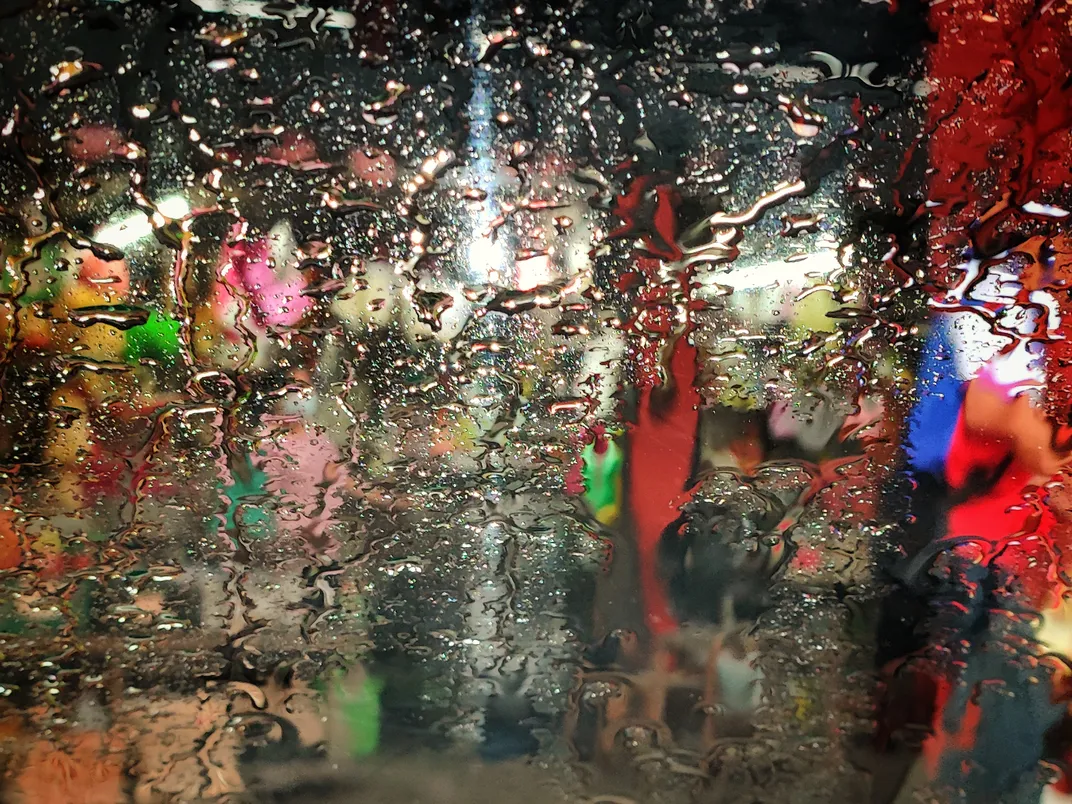 11 - Raindrops on a car windshield blur the outside view of shops of various colors, like paint dripping on a canvas.