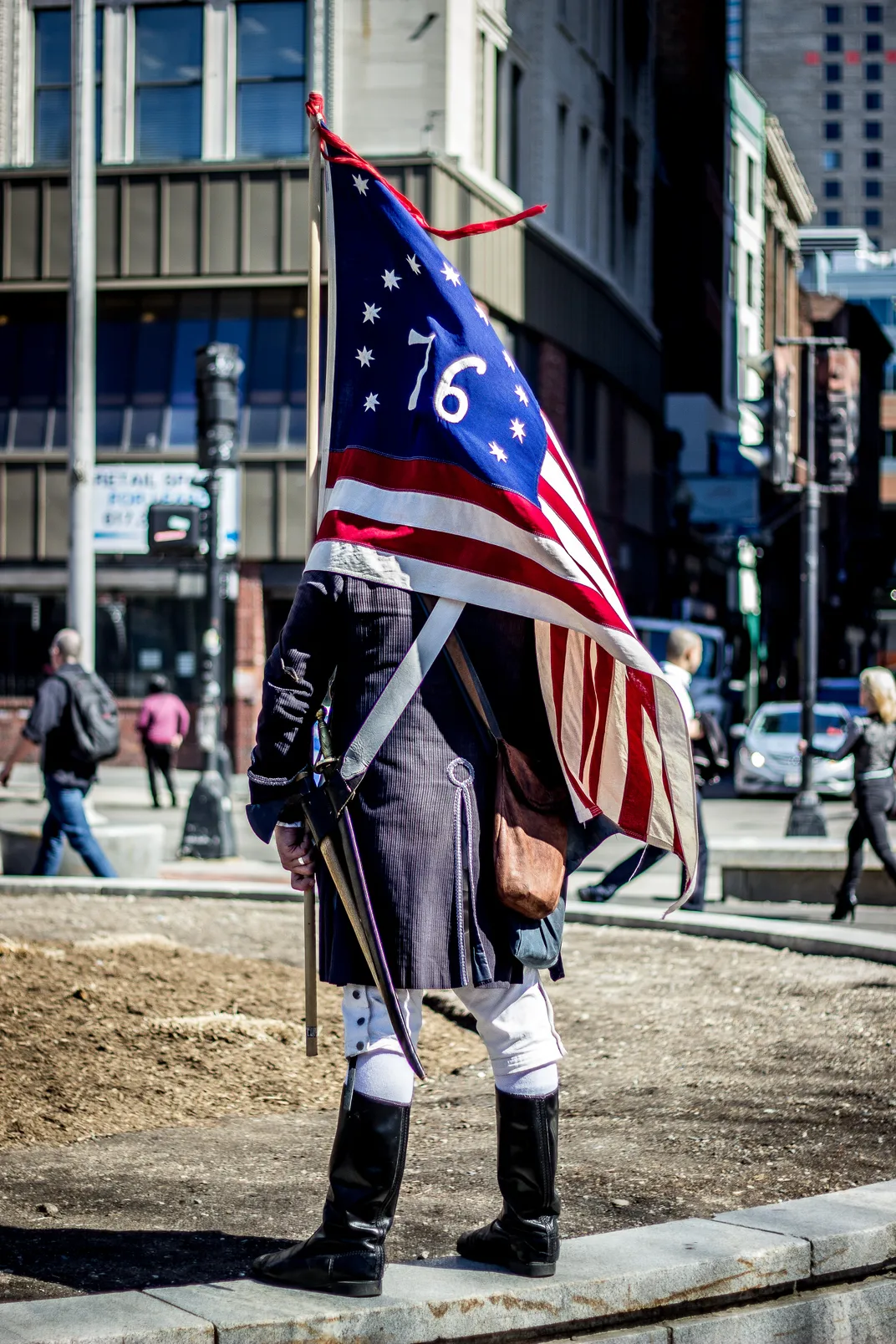 Wearing colonial attire, a man carries a Bennington American flag.