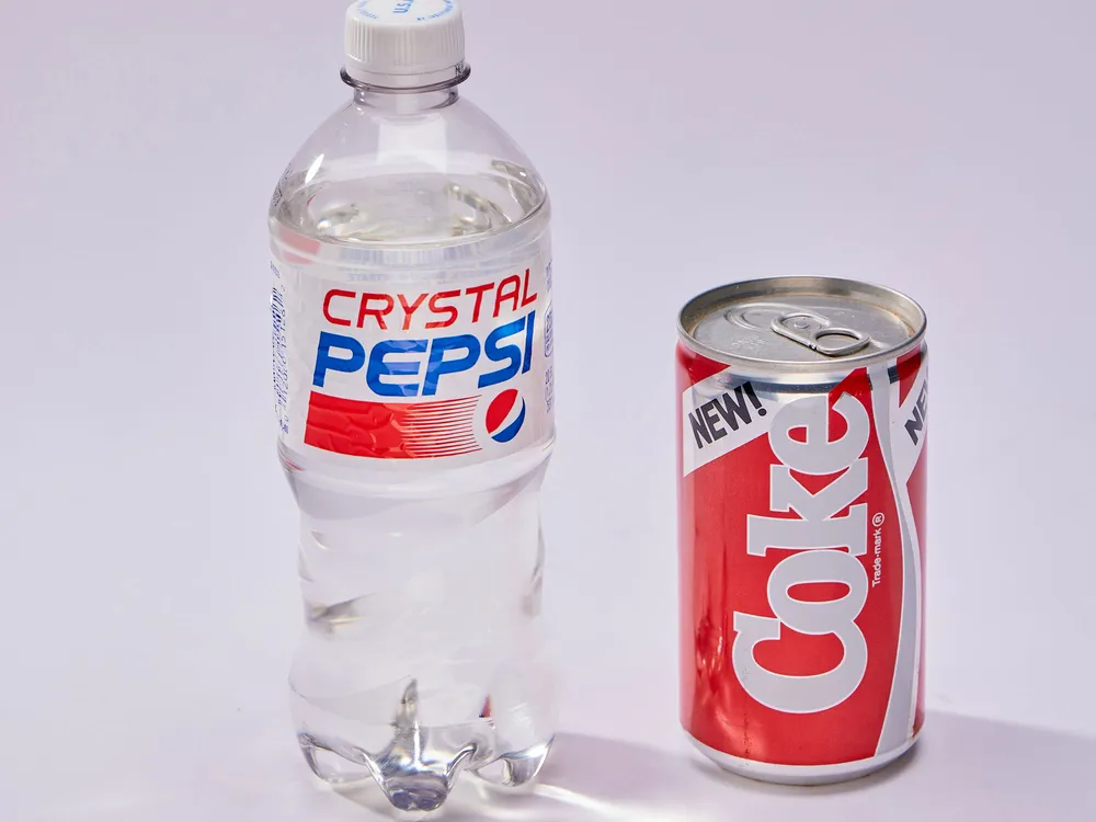 Bottle of clear Crystal Pepsi next to can of New Coke