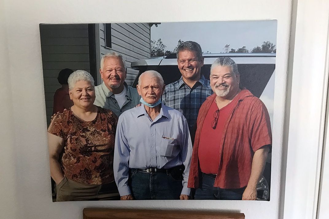 Five adults smiling in a modern color photo, hanging on a white wall above framed photos.