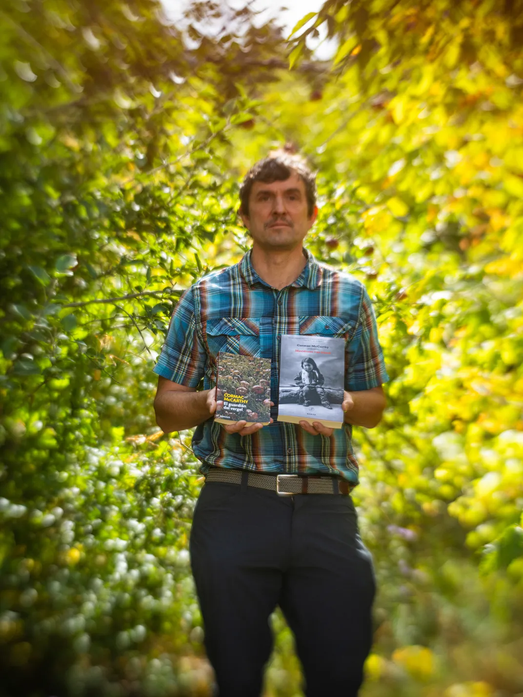 Bryan Giemza, a literary scholar at Texas Tech, by an apple tree in McCarthy’s yard, holding two of the master’s novels—including a Spanish translation of The Orchard Keeper.