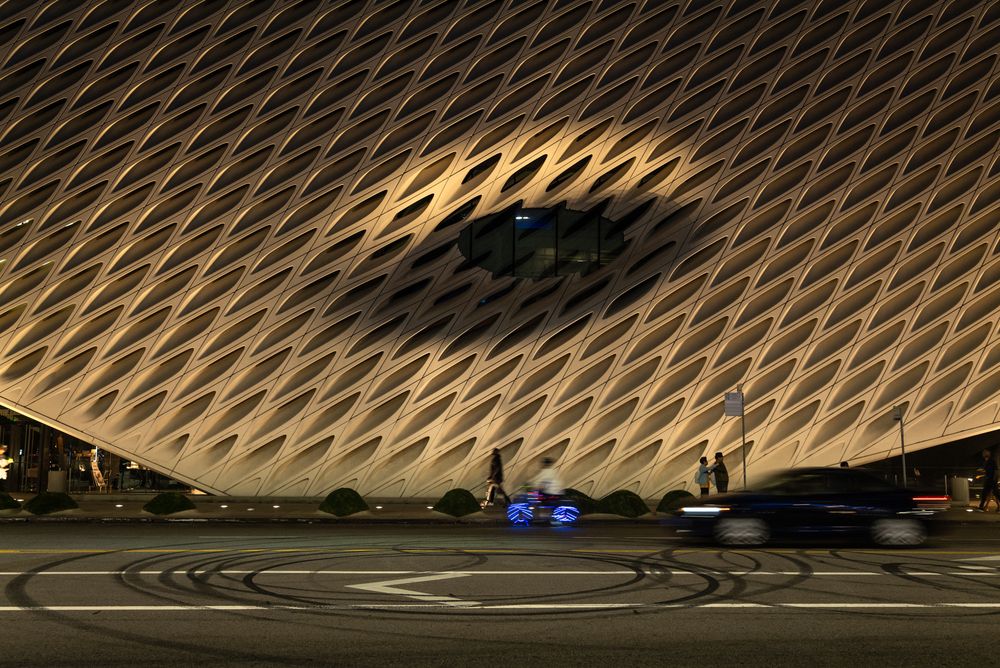 By day or night, the architecture of the Broad Museum in downtown Los Angeles is unique. On this night, it appears as a giant eye looking down on the circular patterns made by tire marks on the street, and dwarfs the passersby.