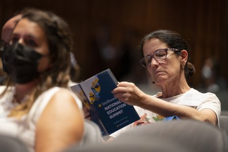 Woman with brown hair and glasses reads through a print program with the words "Smithsonian National Education Summit"