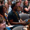 A group of men and women are in an audience turning and talking to each other with smiles