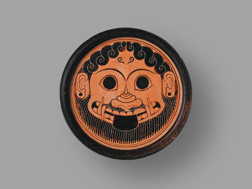 A black and orange stand in a circular shape with a Gorgon's head, including a bear, tusks, large eyes and curled black hair