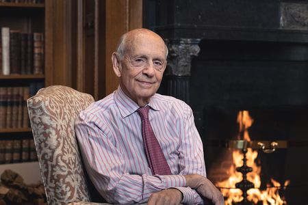 The cover of the book, Reading the Constitution, features Justice Stephen Breyer sitting in front of a blazing fire.