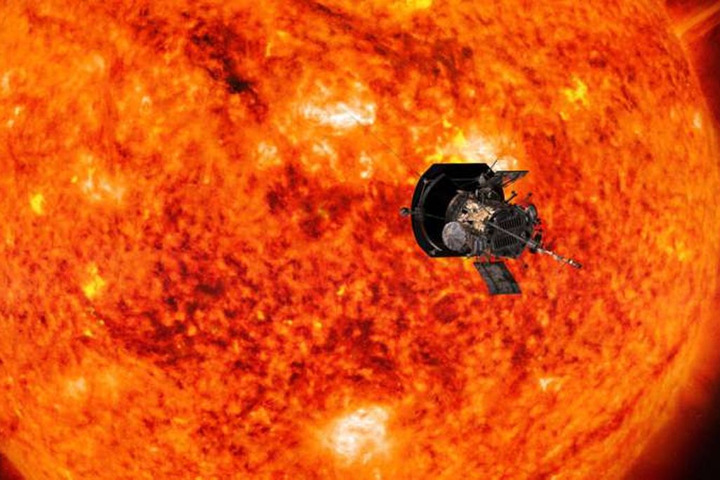 An image of the probe approaching the sun. The sun takes up most of the frame as a glowing, red-orange mass. The probe looks like a small machine approaching its surface.
