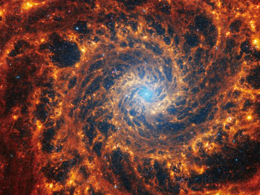In this image of a galaxy, orange wisps spiral out from a small blue center