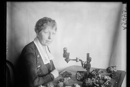 Black and white photo of Margaret W. Moodey sitting at a desk with a microscope and gemstones