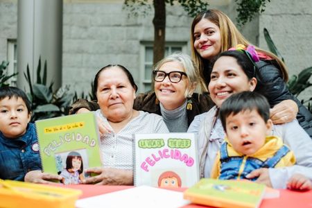 Woman smiles at the center of a group with young children and their mothers showcasing books they created