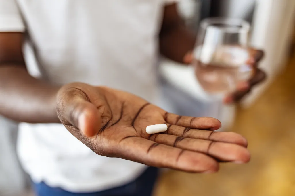 A man holding a white capsule pill and a glass of water