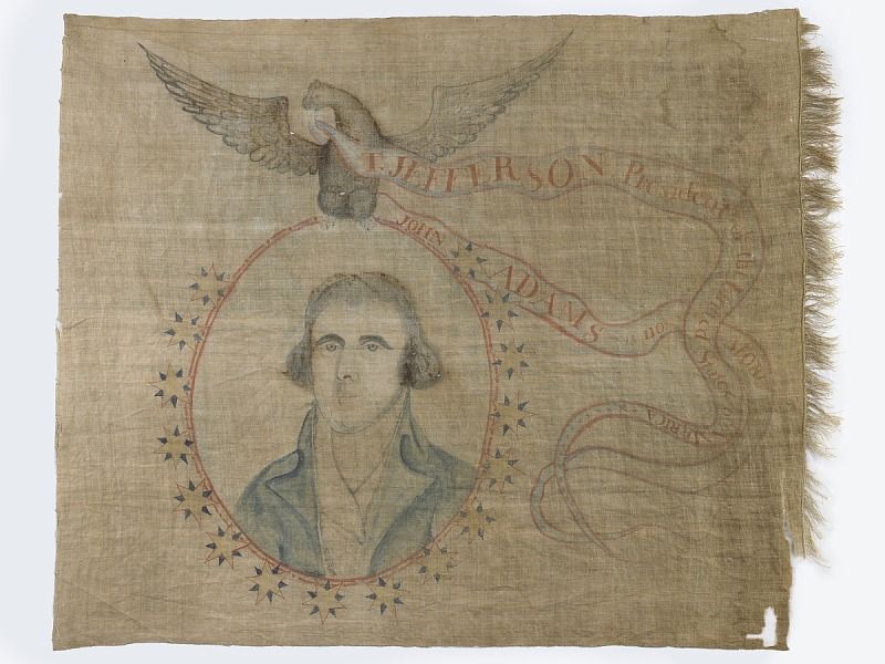 A faded linen banner, frayed on the edges, with a portrait of Jefferson surrounded by a floral garland and an eagle overhead 