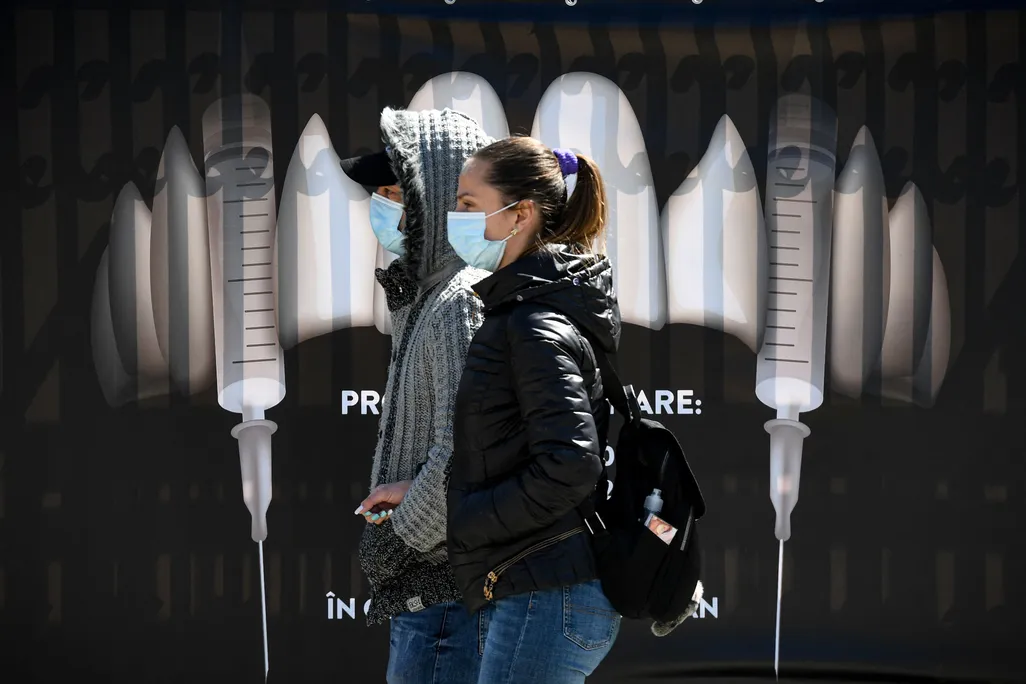 People wearing protection masks walk by a banner showing syringes as vampire fangs during the vaccination marathon organized at the "Bran Castle" in Bran village on May 8, 2021