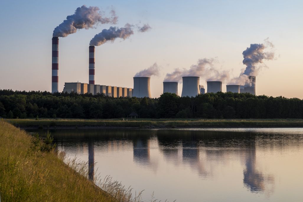 A coal power plant releasing smoke in front of a body of water