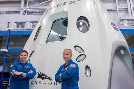 Commercial crew astronauts Bob Behnken (left) and Doug Hurley (right) stand in front of a SpaceX Dragon mock-up at the Johnson Space Center. 