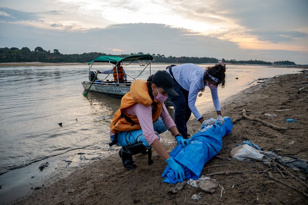 Two women rolling up a blue tarp next to water