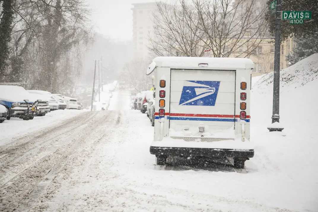 A USPS mail truck sits parked in the snow