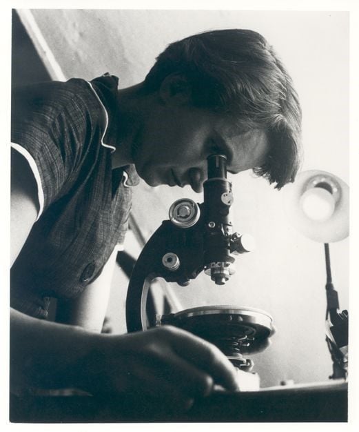 Black and white photo of a woman looking into a microscope.