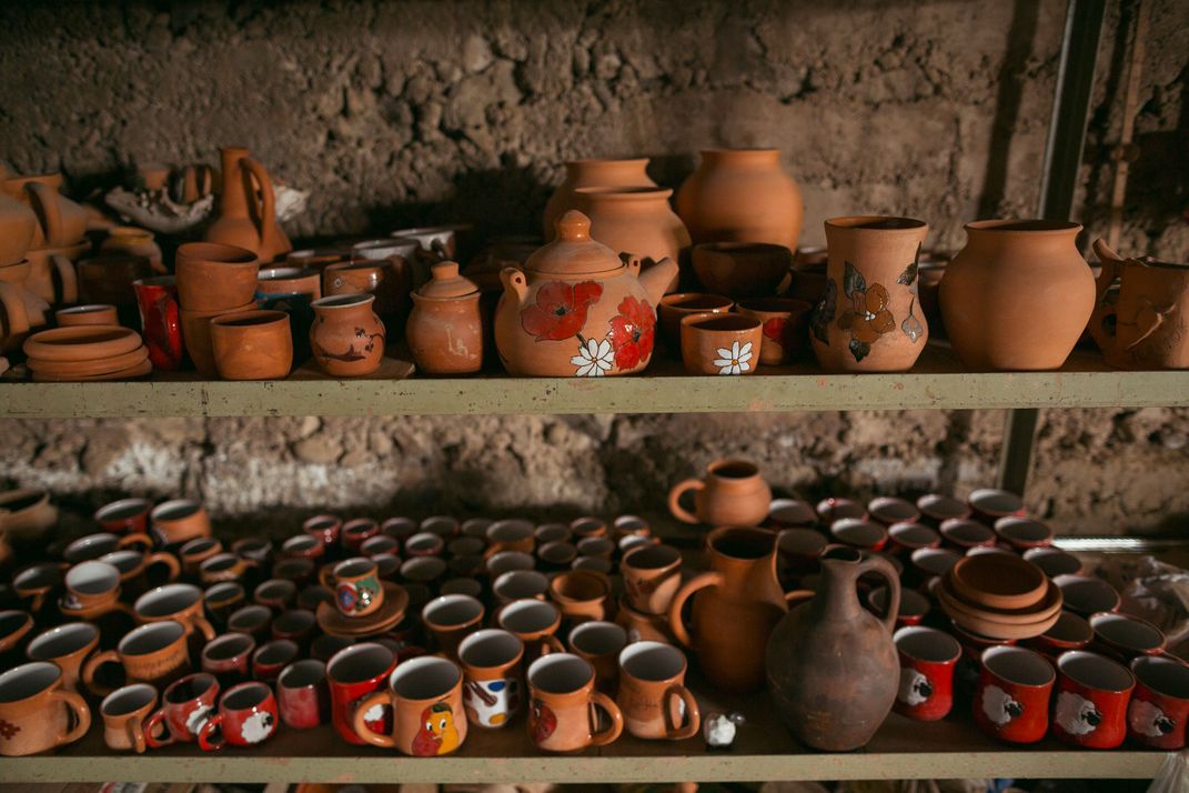 Several rows of teracotta pots are arranged on two shelves, one on top of the other. 