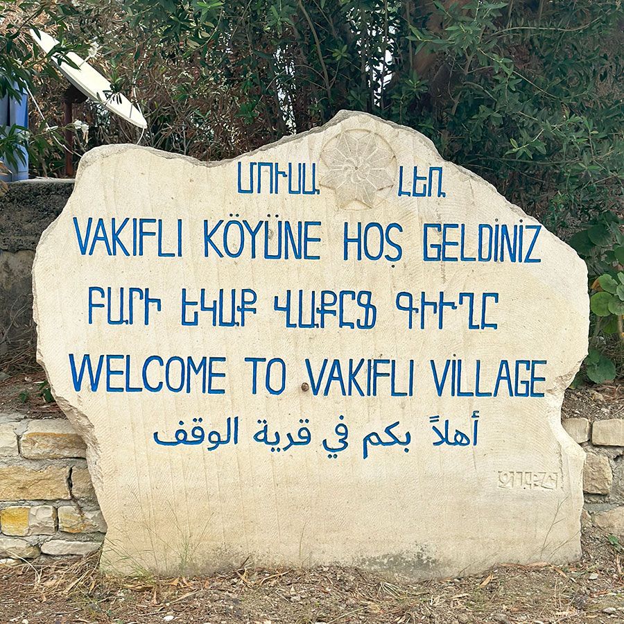 A stone sign with blue lettering in five different languages and scripts. In English: Welcome to Vakifli Village.