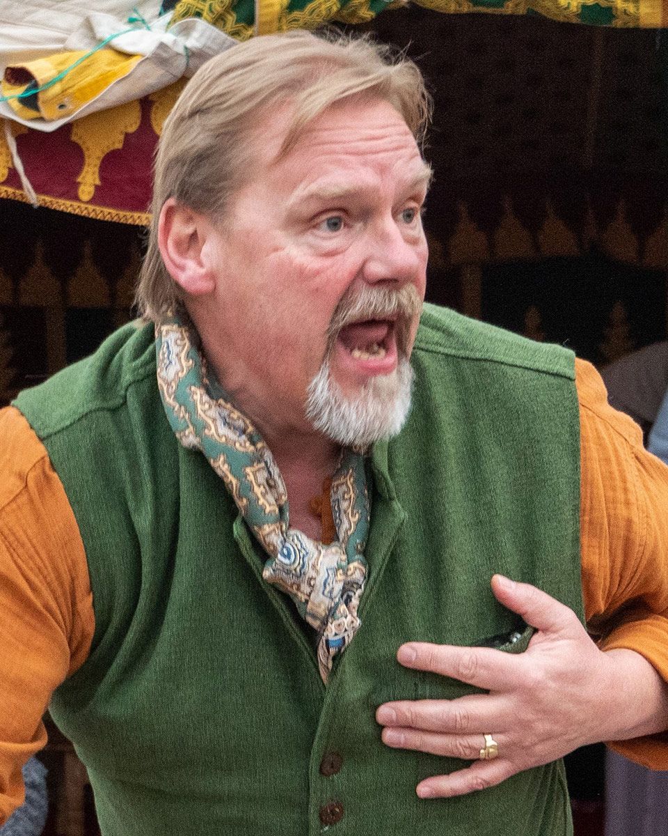 A man with short brown hair and gray goatee tells a story, holding one hand over his heart.