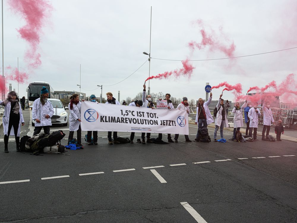 Protesters in Berlin wear white lab coats and hold a sign