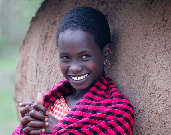 A Smiling Maasai Girl Leaning on Straw and Dung Wall of Hut thumbnail