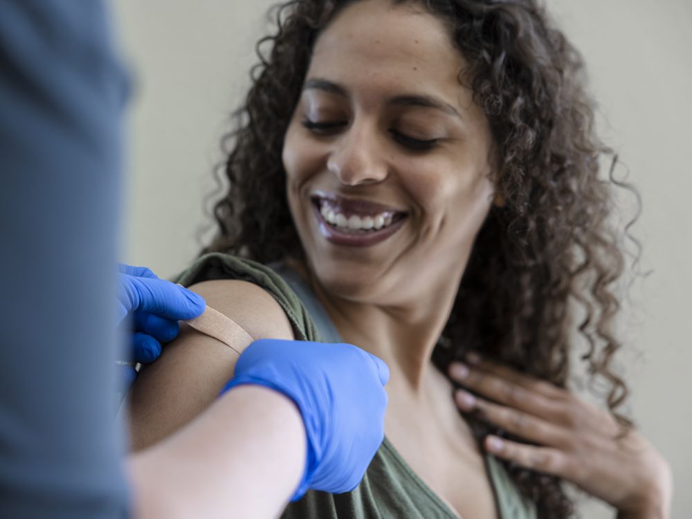 Photo of Black woman receiving a vaccine from a doctor with a bandaid on her arm