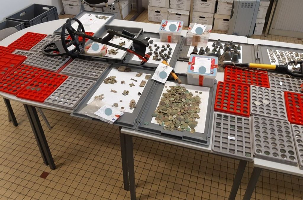 A view of a table covered in piles of coins and other small archaeological artifacts