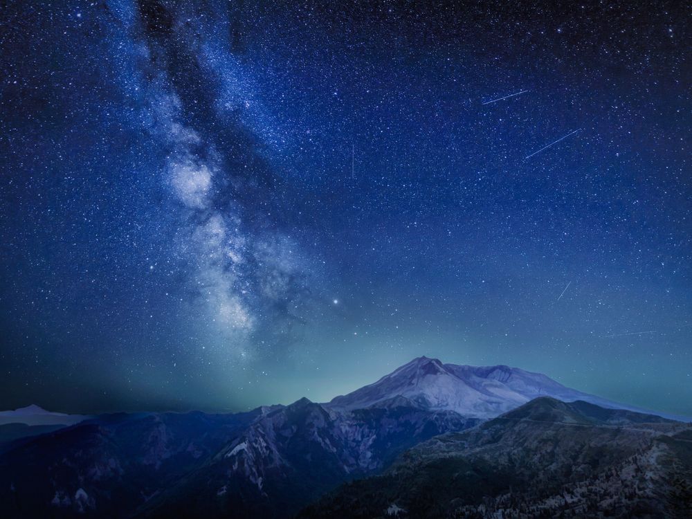 the milky way, several stars, and a few streaks of light left by burning meteors over a mountainous landscape