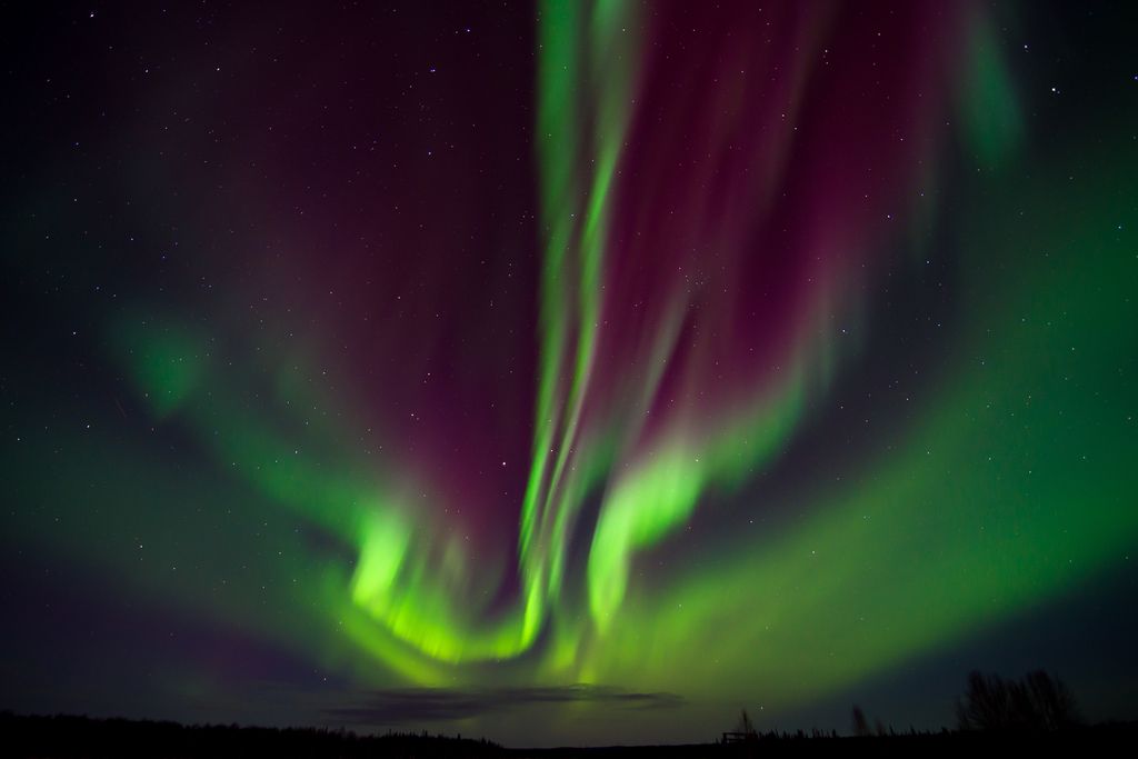 Green and purple northern lights color the night sky above a mountain range