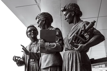 This seven-foot statue of Pearl Kendrick, center, and Grace Eldering, left, was unveiled in Grand Rapids in 2019. Lab assistant Loney Clinton stands to the right with a microscope.